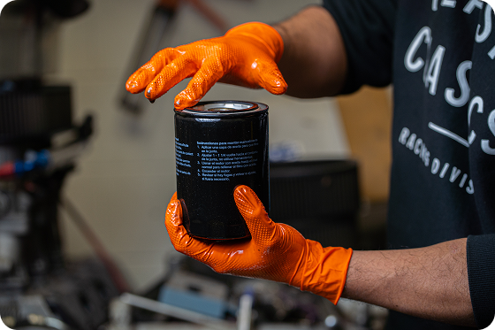 Professional mechanic wearing 8 mil IGRIP orange nitrile gloves with diamond texture for a secure grip on an oil filter.